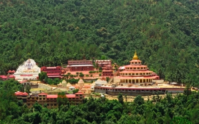 Large, complex ashram structure with a mix of traditional and modern architecture set on a forested hillside